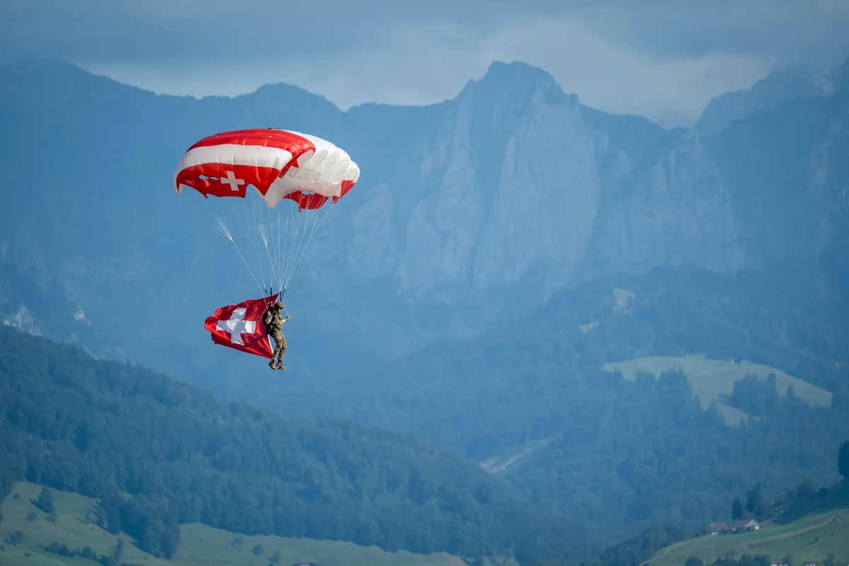 Da kommen Heimatgefühle auf: Ein Fallschirmspringer der Swiss Parawings war mit der Schweizer Flagge vor der Bergkulisse unterwegs. Ein Fallschirmspringer der Armee fliegt in der Luft.